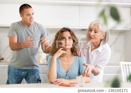 Adult man quarreling with adult and elderly woman in kitchen Adult man quarreling with adult and elderly woman in kitchen 136108171