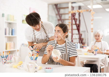 Young ceramicist teaching female novice art of ceramic painting in pottery studio Young ceramicist teaching female novice art of ceramic painting in pottery studio 136108176