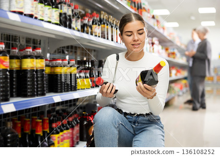 Girl customer is thinking about buying spicy and unusual soy sauce. 136108252