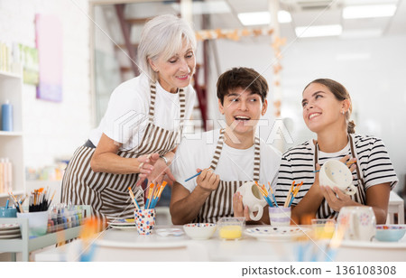 Group of cheerful people painting ceramic dishware in pottery class Group of cheerful people painting ceramic dishware in pottery class 136108308