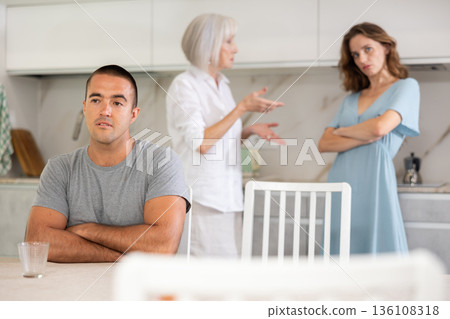 Elderly woman quarrels with couple in kitchen Elderly woman quarrels with couple in kitchen 136108318