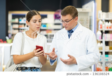 Young girl showing to male pharmacist something displayed on her smartphone 136108324