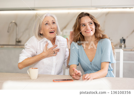 Elderly mother and adult daughter drinking tea and chatting happily Elderly mother and adult daughter drinking tea and chatting happily 136108356