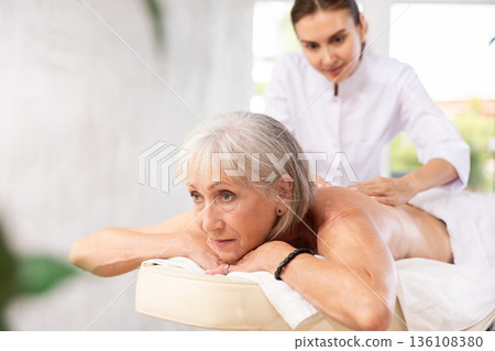 Blurry unrecognizable woman performs shoulder massage to female client. 136108380
