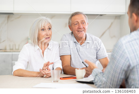 Salesman seller shows on laptop details of purchase to elderly couple. Salesman seller shows on laptop details of purchase to elderly couple. 136108403
