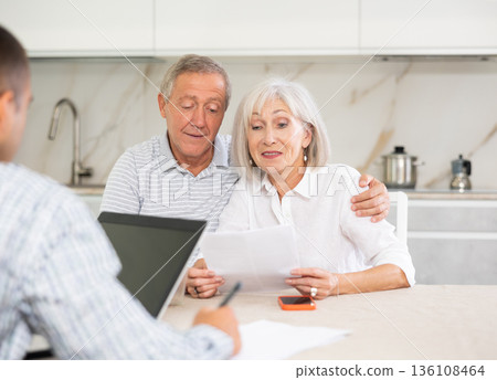 Salesman seller shows on laptop details of purchase to elderly couple. Salesman seller shows on laptop details of purchase to elderly couple. 136108464