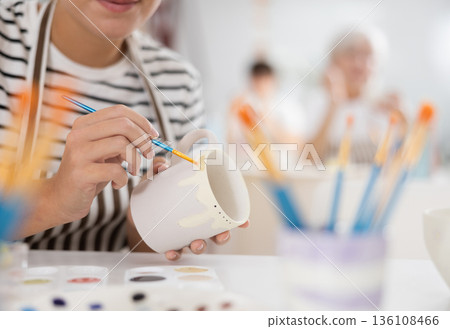 Hands of craftswoman decorating white ceramic mug in pottery workshop Hands of craftswoman decorating white ceramic mug in pottery workshop 136108466