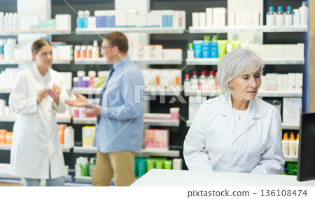 Old female pharmacist looking at display of computer in chemist's shop 136108474