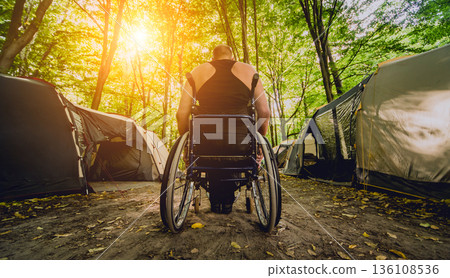 Disabled man resting in a campsite with friends. Wheelchair in the forest  136108536
