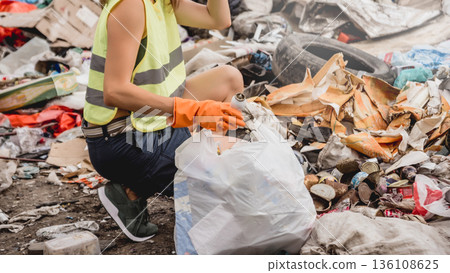 Woman volunteer helps clean the field of plastic garbage.  136108625