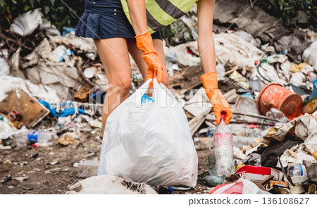 Woman volunteer helps clean the field of plastic garbage.  136108627