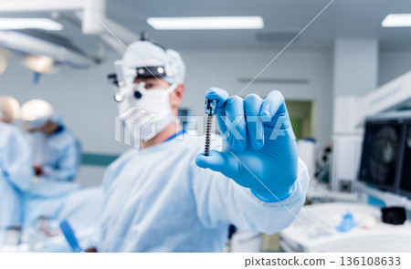 Spinal surgery. Surgeon show polyaxial screw in operating room Spinal surgery. Surgeon show polyaxial screw in operating room 136108633