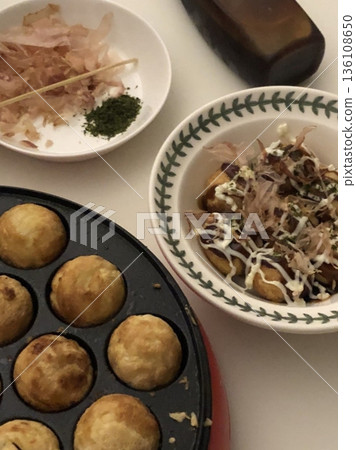 Takoyaki, a popular Japanese street food, are crispy round dough balls filled with octopus, tempura bits, and pickled ginger, topped with takoyaki sauce, bonito flakes, and aonori. 136108650