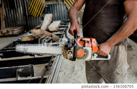 Woodcutter cutting tree with chainsaw on sawmill. Modern sawmill.  136108705