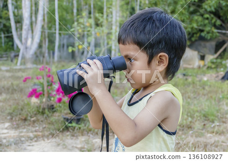 Close up of Asian little cute boy looking through binoculars outdoor over green nature background Close up of Asian little cute boy looking through binoculars outdoor over green nature background 136108927