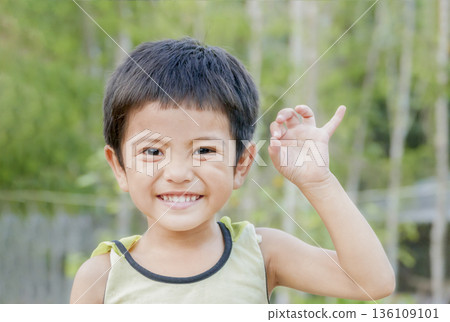 Close up of smiling Asian little cute boy show pinkie finger or reconcile gesture concept and looking at camera outdoor over green nature background Close up of smiling Asian little cute boy show pinkie finger or reconcile gesture concept and looking at camera outdoor over green nature background 136109101