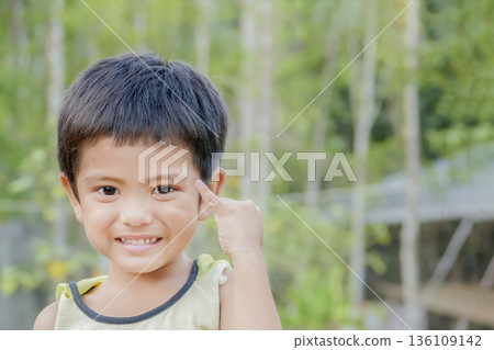 Close up of smiling Asian little cute boy show pinkie finger or reconcile gesture concept and looking at camera outdoor over green nature background Close up of smiling Asian little cute boy show pinkie finger or reconcile gesture concept and looking at camera outdoor over green nature background 136109142