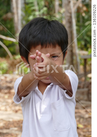 Asian Thai little boy shooting with fingers or making gun gesture in garden Asian Thai little boy shooting with fingers or making gun gesture in garden 136109226