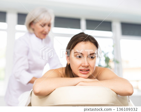 Young woman suffers painful sensations and winces during therapeutic massage session 136109332