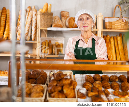 senior bakery worker sells croissants and shows off a variety of crescent-shaped buns. 136109333