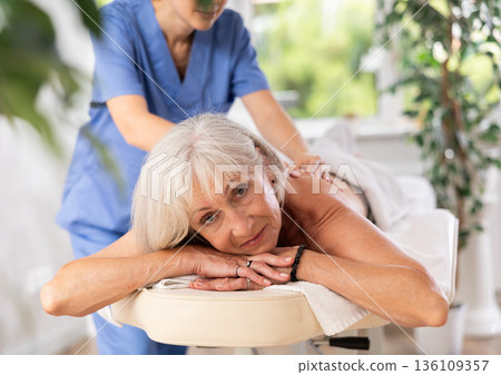 Aged woman relaxing in spa center during professional back massage 136109357