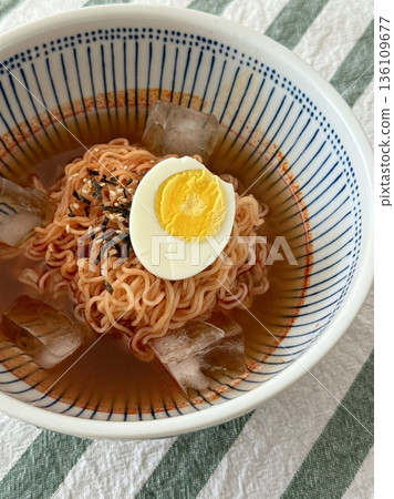 Cold and refreshing Korean naengmyeon noodles, served in a chilled broth with sliced cucumber, radish, and a boiled egg. A savory, tangy dish ideal for hot summer days. 136109677