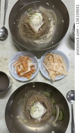 Cold and refreshing Korean naengmyeon noodles, served in a chilled broth with sliced cucumber, radish, and a boiled egg. A savory, tangy dish ideal for hot summer days. Cold and refreshing Korean naengmyeon noodles, served in a chilled broth with sliced cucumber, radish, and a boiled egg. A savory, tangy dish ideal for hot summer days. 136109681
