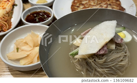 Cold and refreshing Korean naengmyeon noodles, served in a chilled broth with sliced cucumber, radish, and a boiled egg. A savory, tangy dish ideal for hot summer days. 136109682