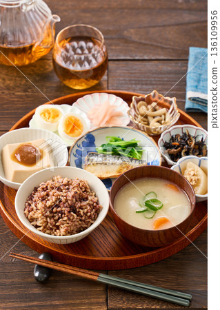 A Japanese breakfast with small dishes: mixed grain rice, miso soup, and grilled salted mackerel 136109956
