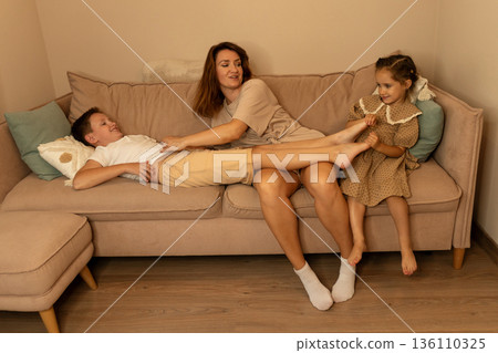 Mother and children relaxing together on sofa Mother and children relaxing together on sofa 136110325