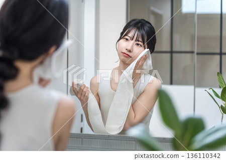 一位年輕的亞洲女性洗完臉後對著鏡子檢查皮膚（皮膚問題、乾燥、護膚、皮膚問題） 136110342