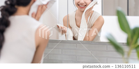A young Asian woman towel-drying her face after washing it in front of a mirror (skin care, face care) A young Asian woman towel-drying her face after washing it in front of a mirror (skin care, face care) 136110511