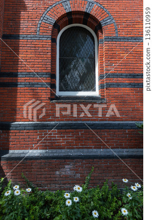 Arched glass window on old red brick house. Vintage brick wall with window and flowers in front 136110959