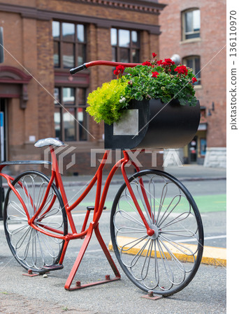 Beautiful red painted bicycle front wheel with a bucket of colorful flowers on the city street 136110970
