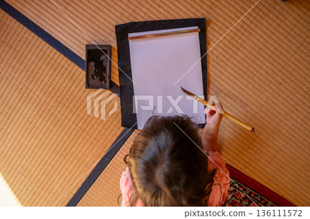 一個女孩在榻榻米上寫書法。 136111572