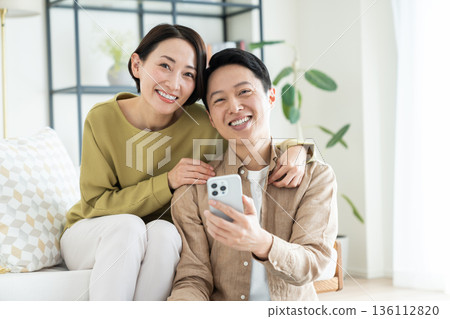 A middle-aged couple watching a smartphone in the living room A middle-aged couple watching a smartphone in the living room 136112820