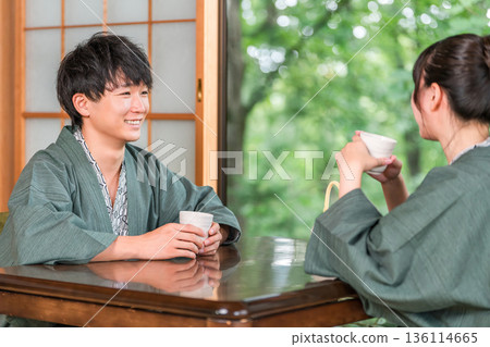 A couple in yukata drinking tea in a Japanese-style room at a ryokan with a garden view A couple in yukata drinking tea in a Japanese-style room at a ryokan with a garden view 136114665