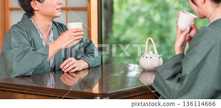 A couple in yukata drinking tea in a Japanese-style room at a ryokan with a garden view A couple in yukata drinking tea in a Japanese-style room at a ryokan with a garden view 136114666