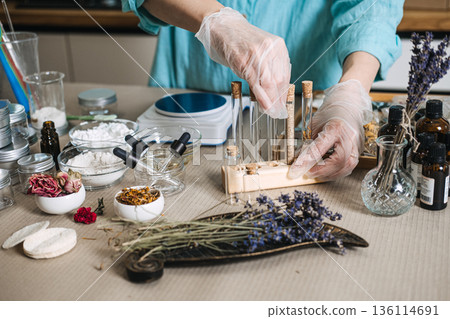 Person wearing gloves organizes glass test tubes filled with dried botanicals in wooden rack on workshop table. self-care vial set, bath ritual kit, daily wellness shot, curated spa gift. Person wearing gloves organizes glass test tubes filled with dried botanicals in wooden rack on workshop table. self-care vial set, bath ritual kit, daily wellness shot, curated spa gift. 136114691