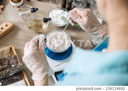Hands in gloves use dropper and glass rod to mix powder in bowl on electronic scale. Pharmaceutical-grade DIY, wellness technology, bio-hacking beauty, at-home lab equipment. Hands in gloves use dropper and glass rod to mix powder in bowl on electronic scale. Pharmaceutical-grade DIY, wellness technology, bio-hacking beauty, at-home lab equipment. 136114692