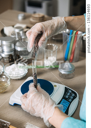 Top view of person pouring dark botanical ingredients from one test tube into another on digital scale. Boutique beauty production, micro-manufacturing, scaling a handmade brand. Top view of person pouring dark botanical ingredients from one test tube into another on digital scale. Boutique beauty production, micro-manufacturing, scaling a handmade brand. 136114693