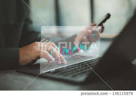 Businessperson analyzing stock market data on laptop with smartphone technology Businessperson analyzing stock market data on laptop with smartphone technology 136115879