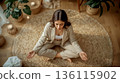 Young woman yoga meditating in a cozy room with a rug and candles. Peaceful atmosphere for mindfulness and stress relief. Concept of wellness, relaxation, mental health, and meditation practice. 136115902