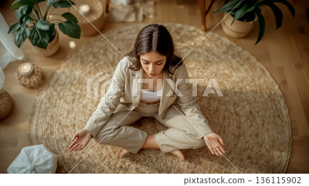 Young woman yoga meditating in a cozy room with a rug and candles. Peaceful atmosphere for mindfulness and stress relief. Concept of wellness, relaxation, mental health, and meditation practice. 136115902