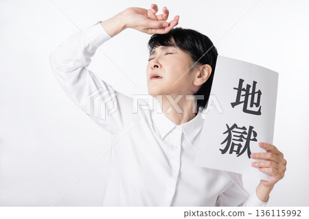 A senior woman lamenting and holding a piece of paper with the word "Hell" written on it 136115992
