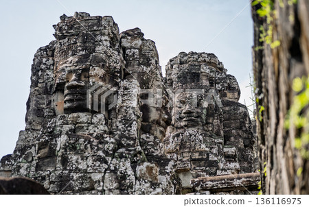 Close up view of giant smiling stone faces carved on towers of ancient Bayon temple in Angkor Thom complex Cambodia 136116975