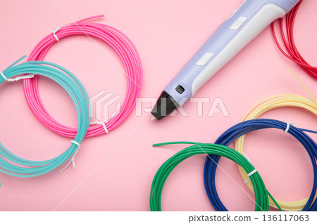 Children's 3D handle with plastic coils red, white, yellow, blue on pink background. Plastic PLA and ABS filament material for printing on a 3D pen Children's 3D handle with plastic coils red, white, yellow, blue on pink background. Plastic PLA and ABS filament material for printing on a 3D pen 136117063