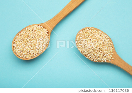 Pile of raw quinoa seeds in wooden spoon on blue background, top view. Pile of raw quinoa seeds in wooden spoon on blue background, top view. 136117086