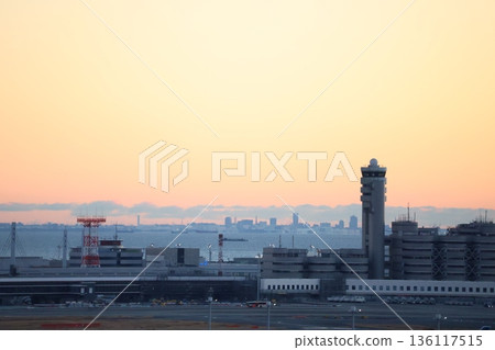 A view of the morning sky, the control tower, buildings, runway, airport, sea, ships, and a hazy cityscape A view of the morning sky, the control tower, buildings, runway, airport, sea, ships, and a hazy cityscape 136117515