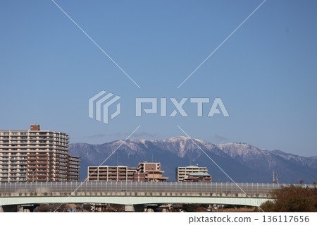 A view of a highway bridge, a town of apartment buildings, snow-capped mountains and blue sky 136117656